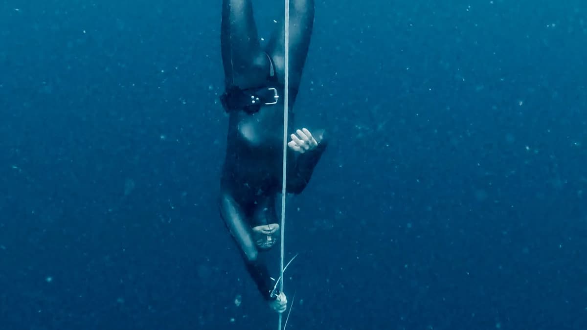 Freediver descending deep on a line in dark blue water