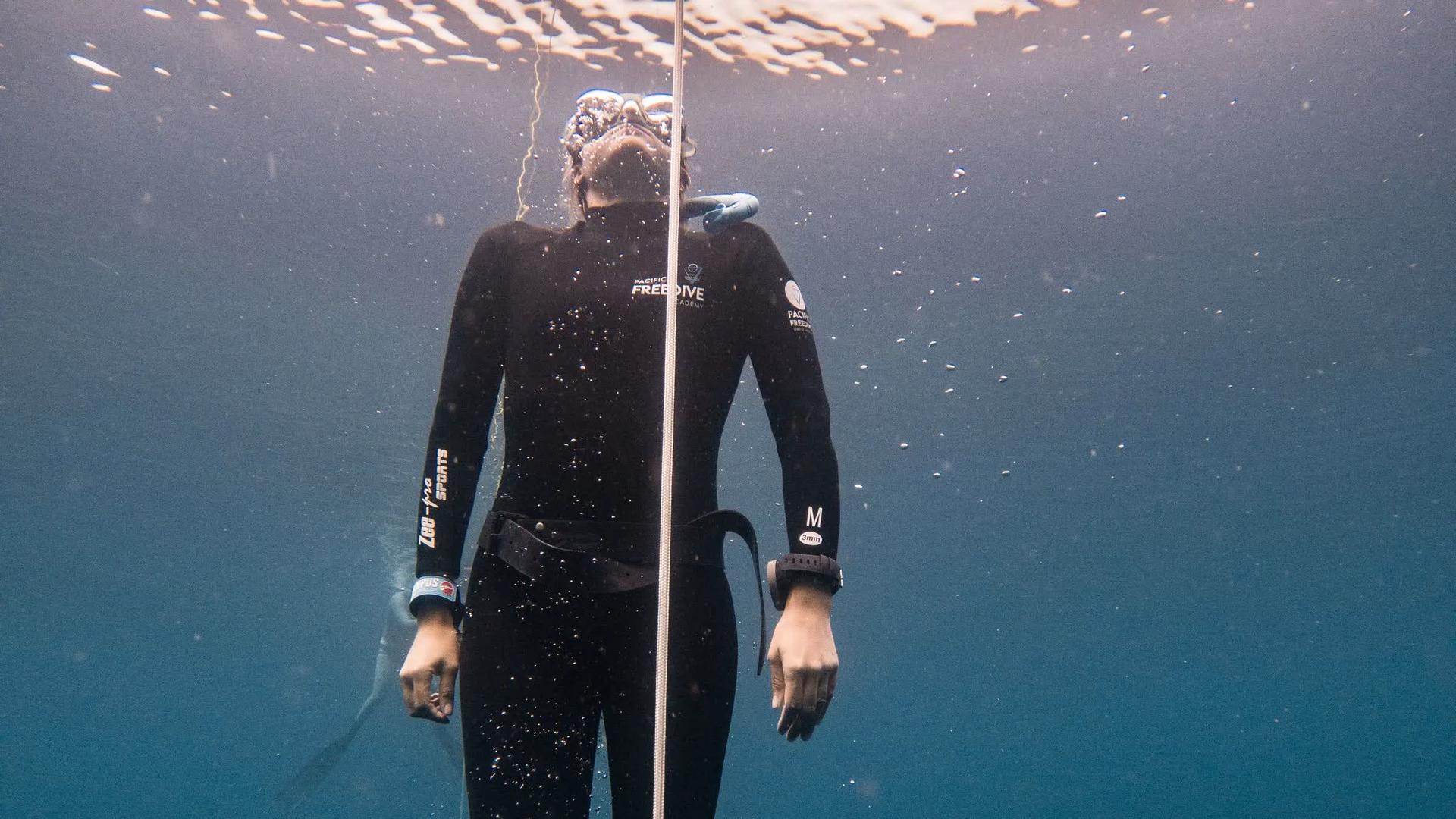 Freediver ascending calmly along a line near the surface