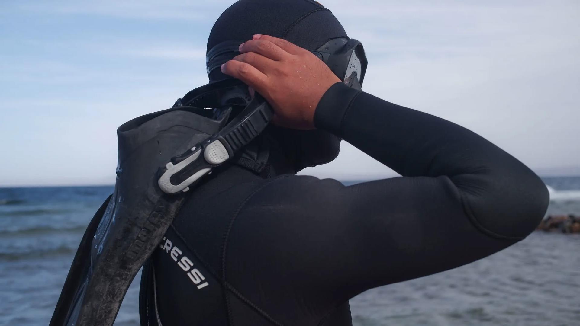 Freediver adjusting mask and hood before entering the water, fins over shoulder