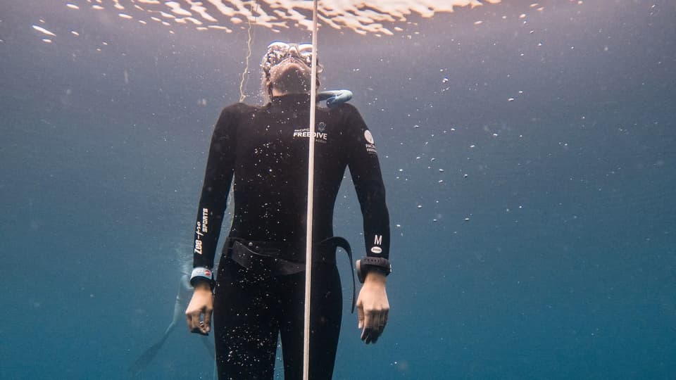 Freediver ascending calmly along a line near the surface