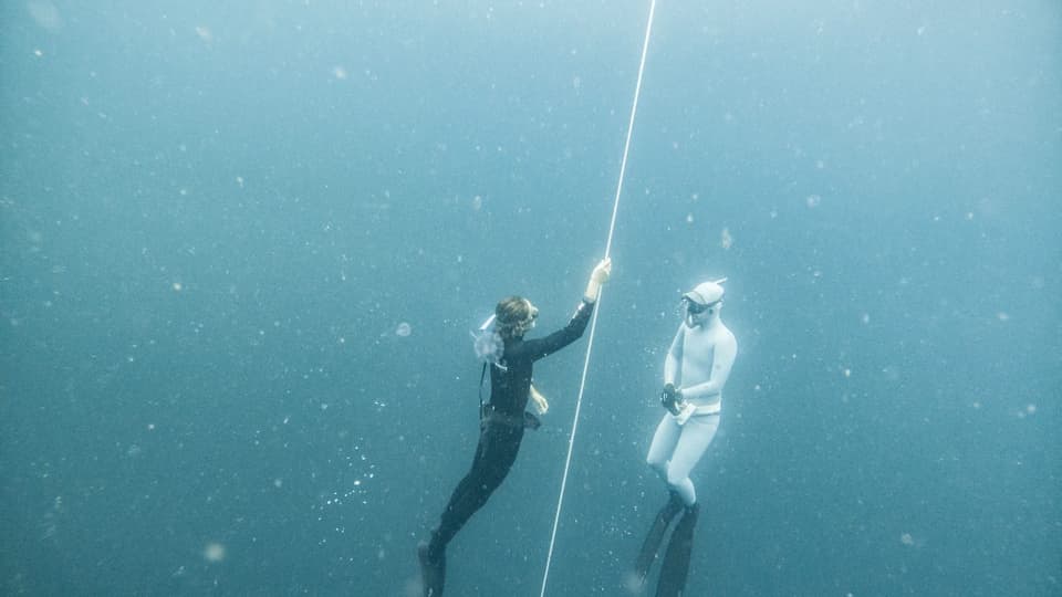 Two freedivers on a descent line, one holding the rope and watching the other