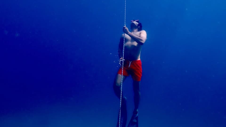 Freediver with bifins ascending a line in deep blue water