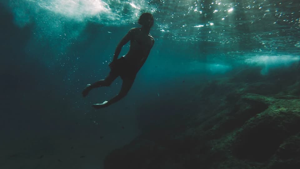 Cinematic silhouette of a diver underwater with light rays