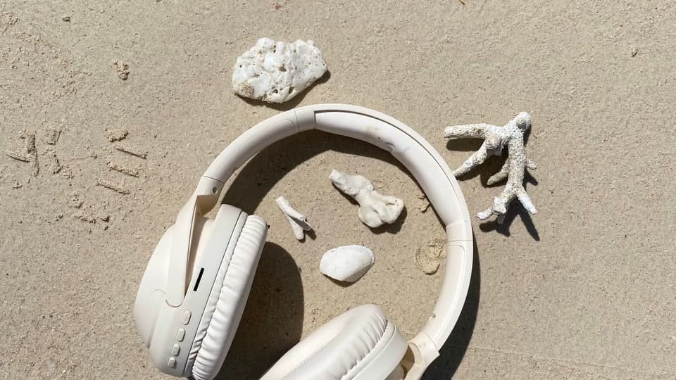 White headphones on a sandy beach next to pieces of coral