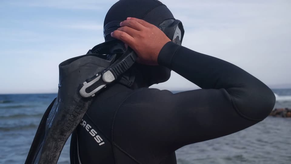 Freediver adjusting mask and hood before entering the water, fins over shoulder