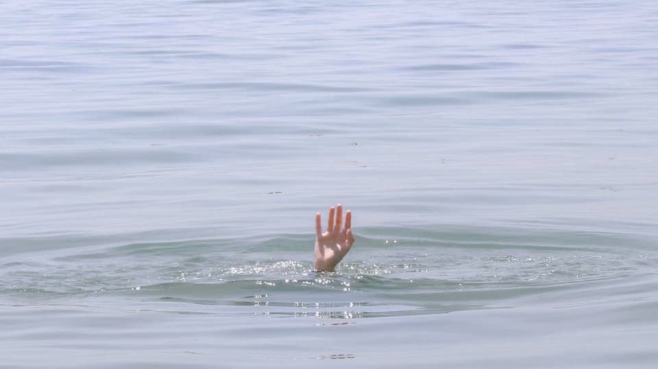 A hand reaching up from the surface of calm water