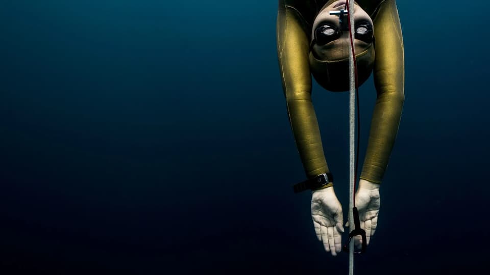 Freediver descending a line with hands framing the face, equalizing