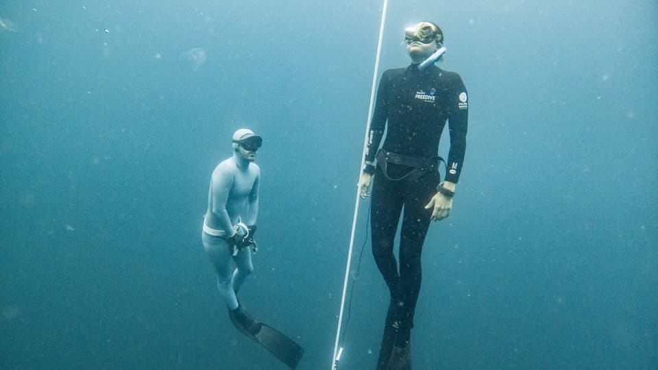 A freediving instructor and student on a descent line underwater