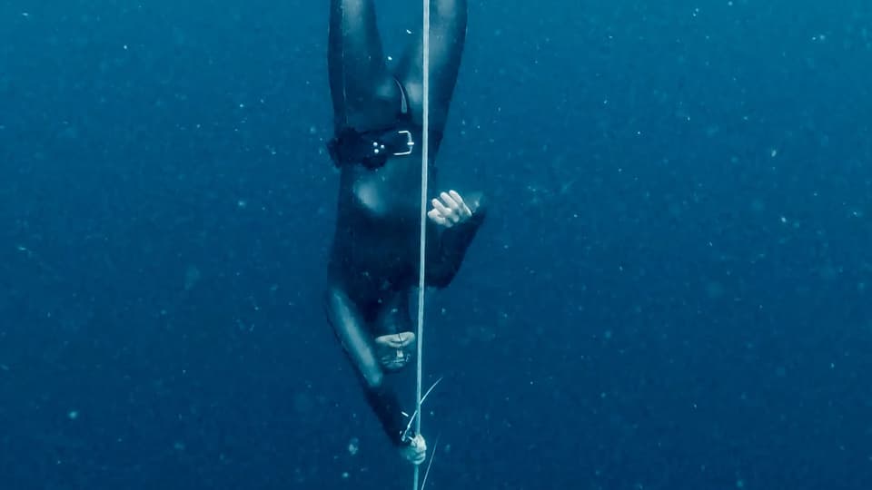 Freediver descending deep on a line in dark blue water